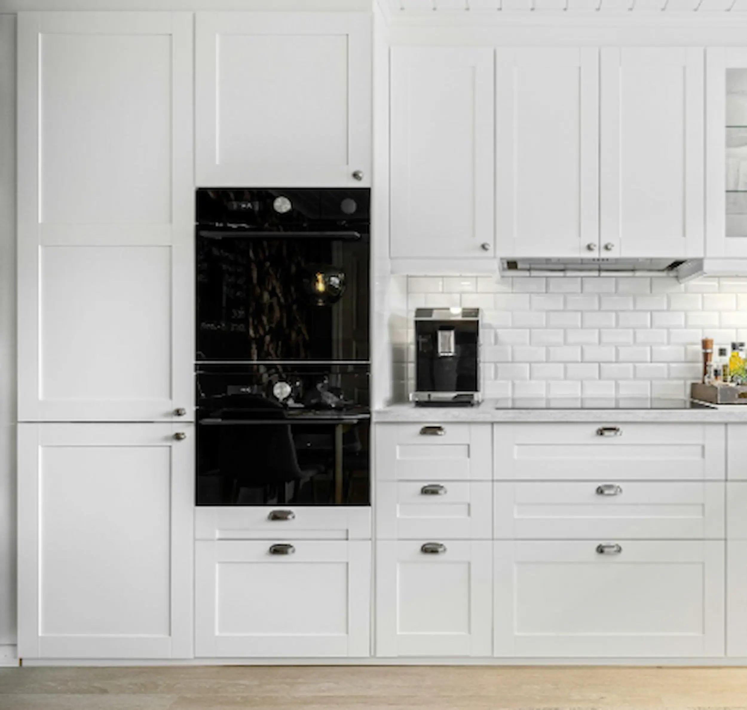 Vaalea keittiö, jossa on valkoiset kaapistot, integroidut kodinkoneet ja työtasolle sijoitettu aamiaiskaappi kahvikoneelle.