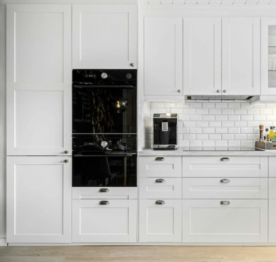 Vaalea keittiö, jossa on valkoiset kaapistot, integroidut kodinkoneet ja työtasolle sijoitettu aamiaiskaappi kahvikoneelle.