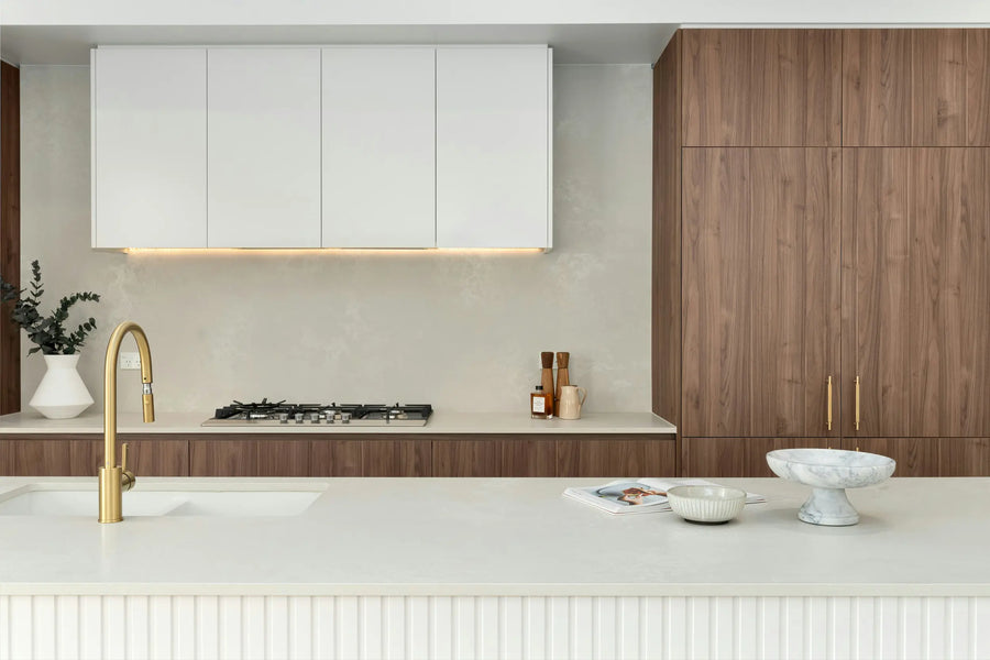 Vaalea kivitaso modernissa keittiössä, jossa puunsävyiset kaapistot, valkoinen allas ja messinkinen hana.