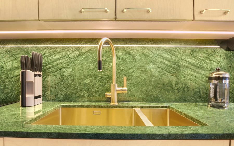 Moderni keittiö, jossa vihreä luonnonkivinen taso ja tausta, kultainen allas ja hana sekä veitsiteline työpöydällä.