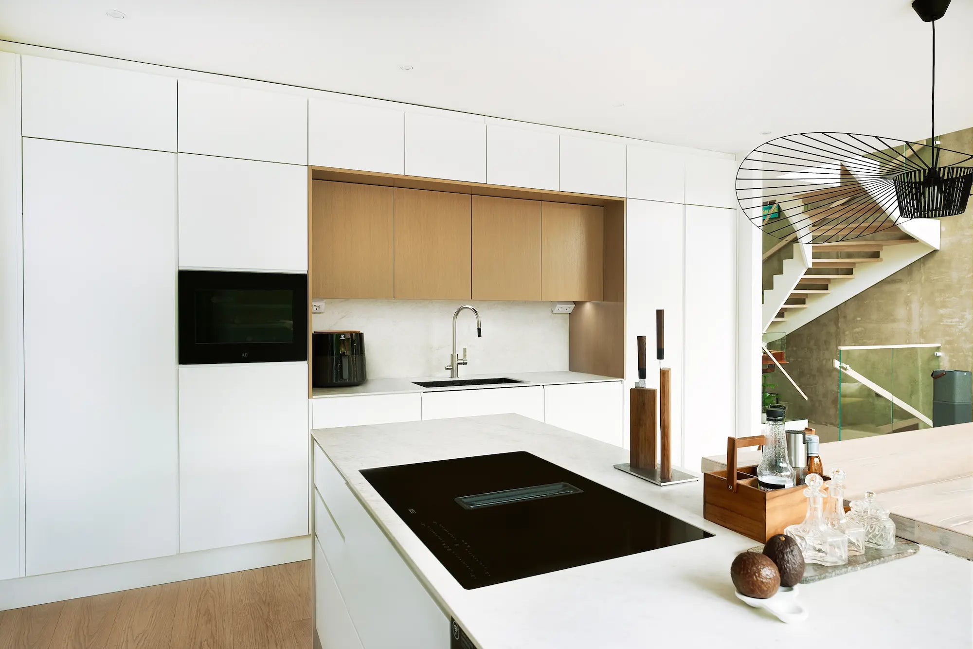 Vaalea ja ajaton keittiö, jossa valkoiset mattapintaiset ovet, tammiviilu ja marmorikuosinen työtaso. Saarekkeellinen keittiö avautuu ruokailu- ja oleskelutilaan ja portaisiin.