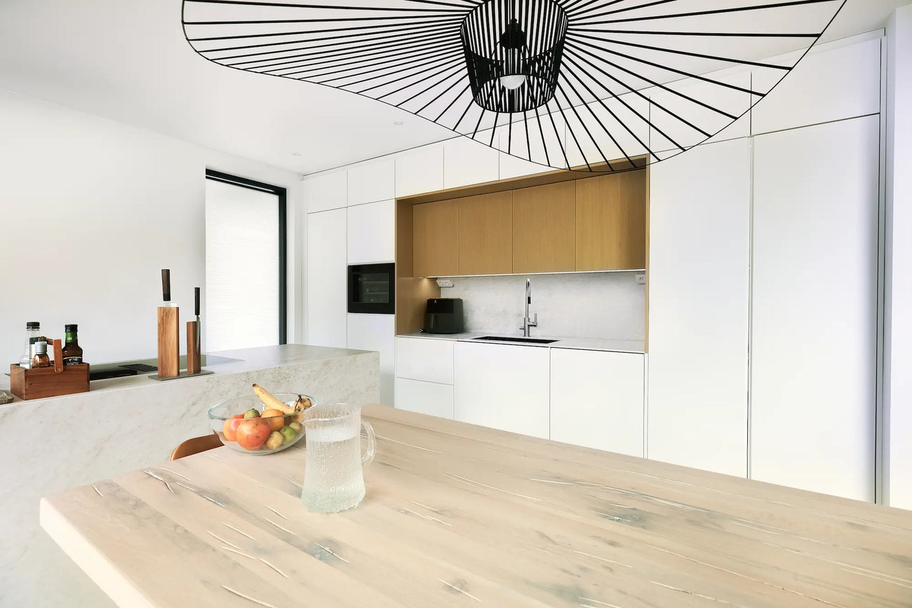  Moderni keittiö ja ruokailutila, joissa vaaleat pinnat, luonnonmateriaalit muodostavat minimalistisen tyylin. Saareke toimii tilan keskuksena.
