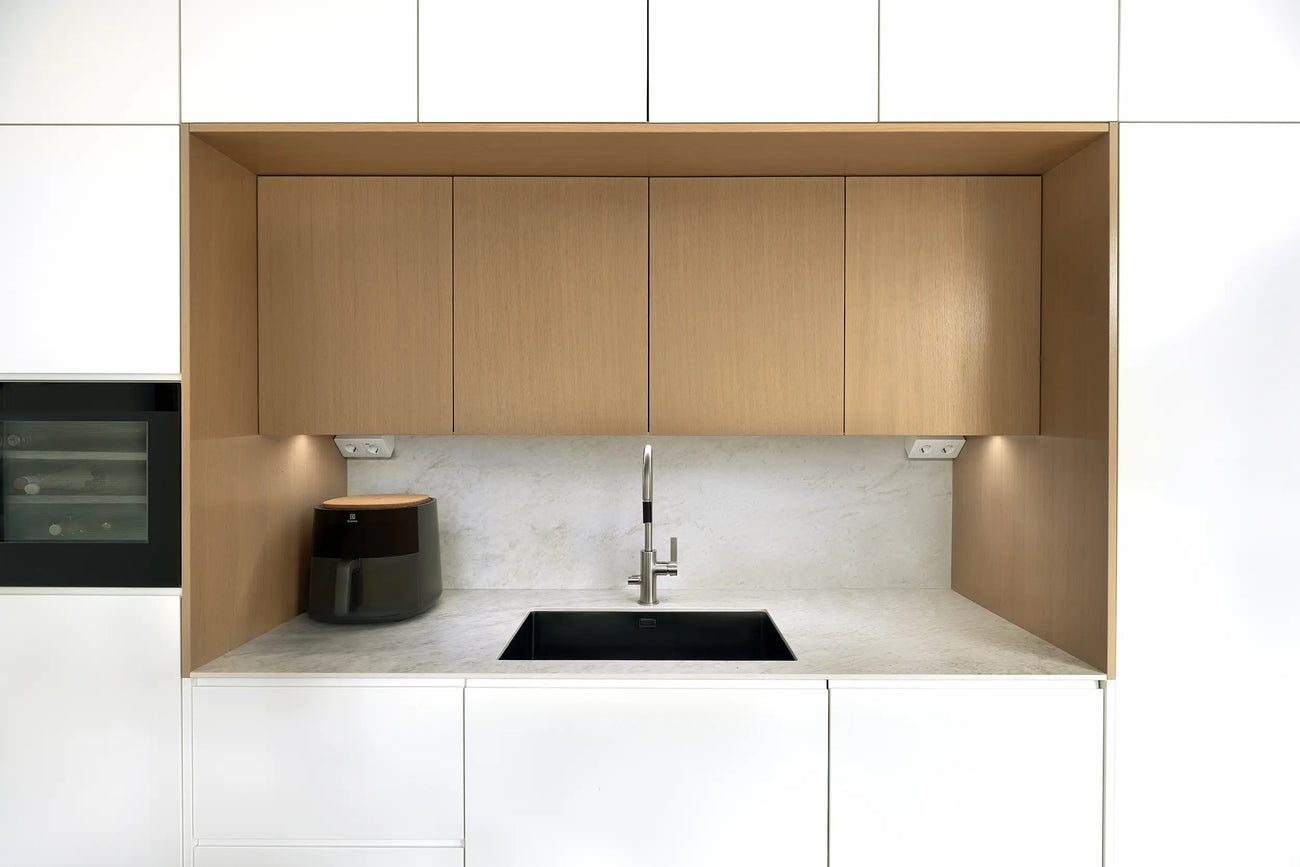 Lähikuva keittiön allasalueesta, jossa tammiviiluiset yläkaapit, marmorikuosinen työtaso ja musta allas luovat rauhallisen, harmonisen kokonaisuuden.